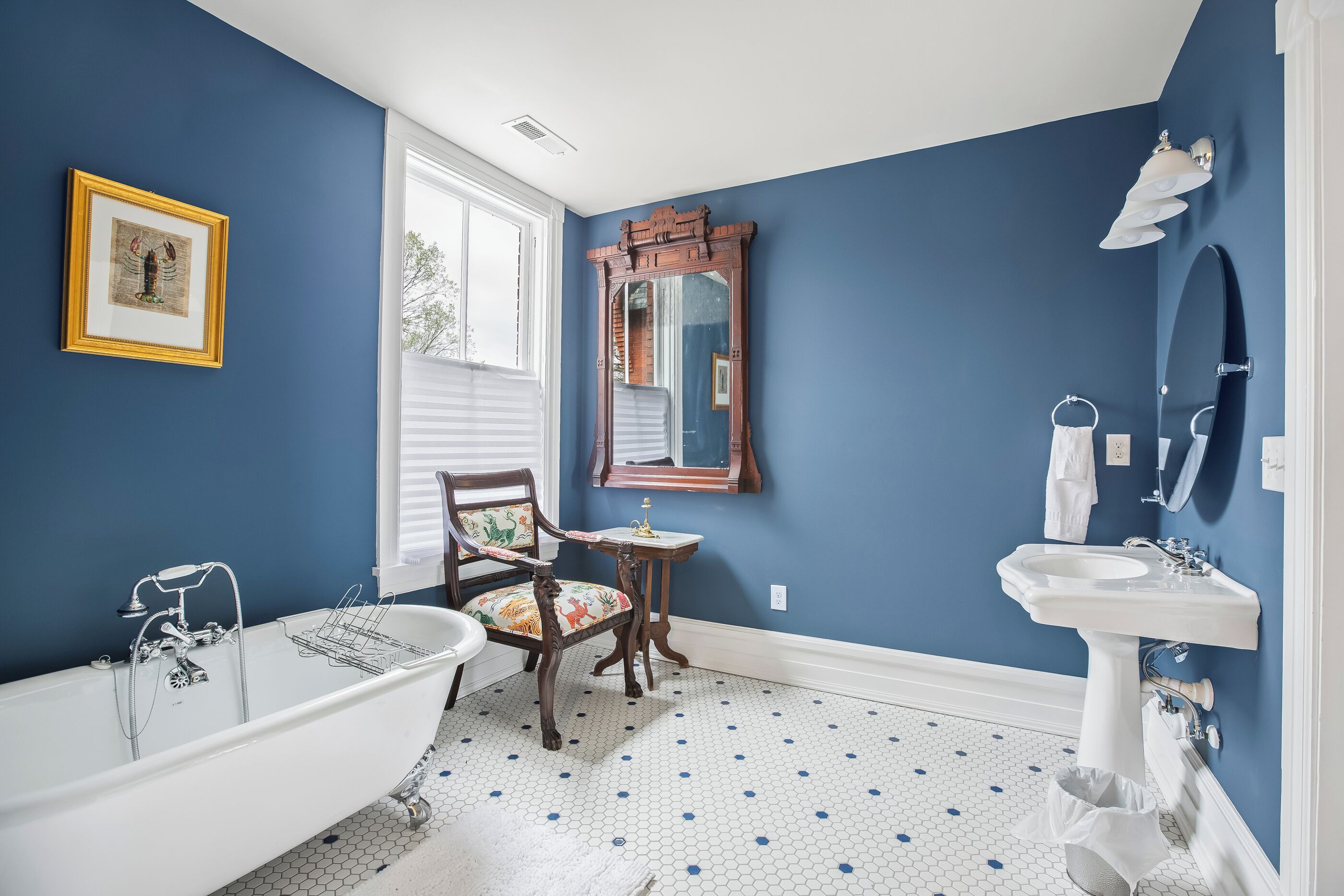 A bathroom with a clawfoot bathtub, a wooden chair, a mirror, and a sink.