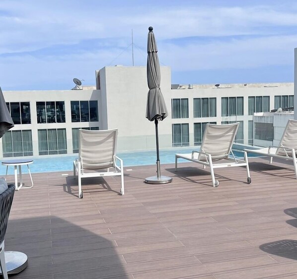 Un espace piscine aménagé sur le toit, avec des chaises longues et un parasol.
