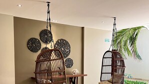 A modern lobby with two hanging wicker chairs, a wooden table, decorative wall art, and a small indoor garden. - Departamento con Jacuzzi en Playa del Carmen  (Playa del Carmen)