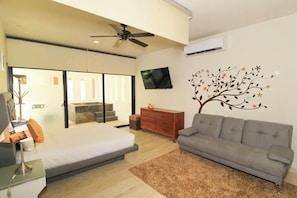 A modern bedroom with a bed, a grey sofa, a TV, and a decorative tree wall decal.