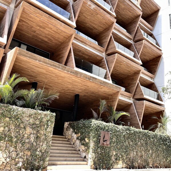 A modern building with a unique geometric facade, featuring multiple balconies and a stone staircase leading to the entrance.