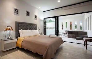 A modern bedroom with a large bed, a nightstand, a lamp, and a view of a balcony with plants. - Departamento con Jacuzzi en Playa del Carmen  (Playa del Carmen)
