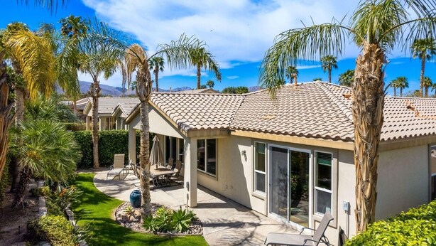 A residential property with a patio, outdoor seating, and palm trees.