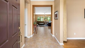 A hallway with a wooden door, beige walls, and a view into a living area with a sofa and a table.