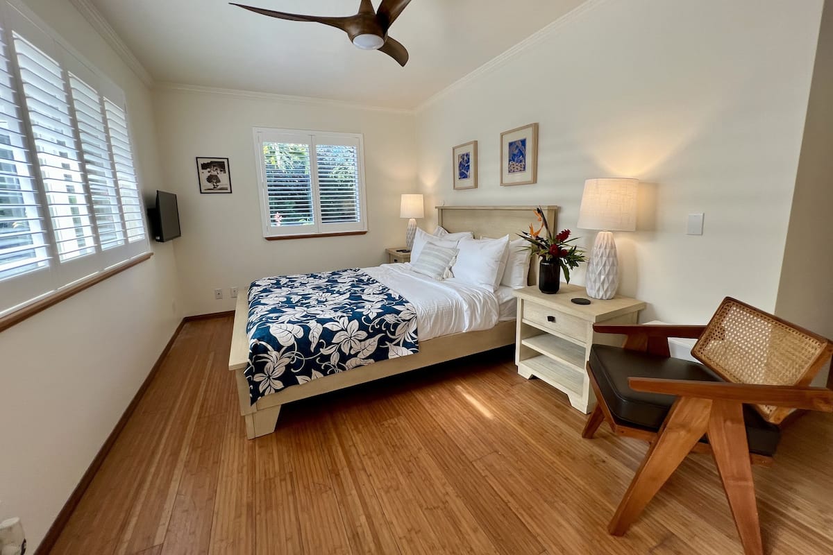 A bedroom with a bed, bedside tables, a chair, a ceiling fan, and a window with blinds.