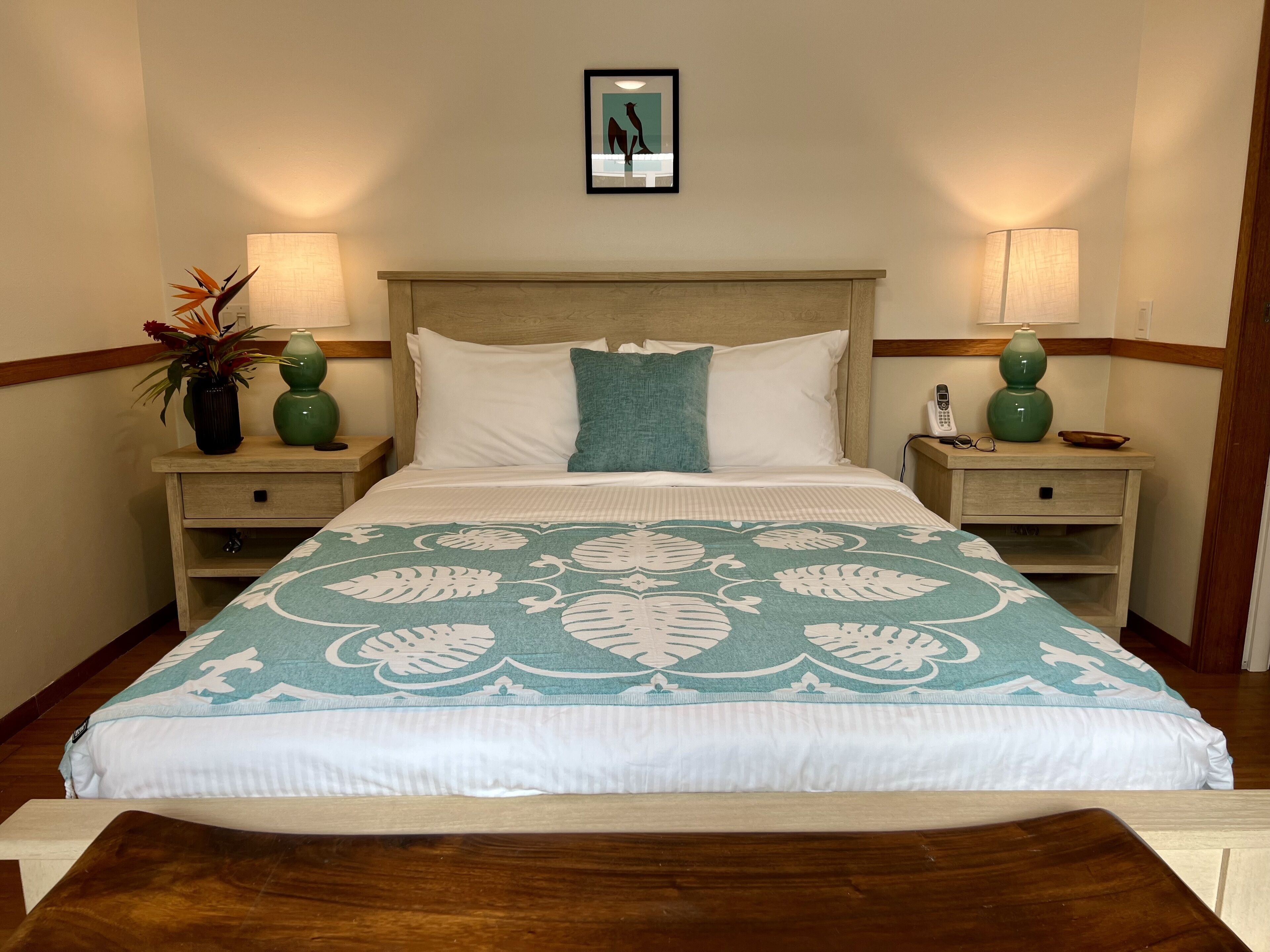 A neatly made bed with a floral bedspread, two bedside tables with lamps, and a framed picture on the wall.