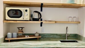 A kitchen with a microwave, kettle, and shelf with dishes and jars. - Mango Sunset Bed and Breakfast (Kailua-Kona)
