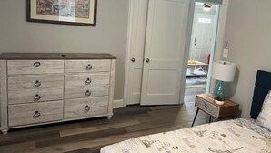 A bedroom with a wooden dresser, a bed with a patterned bedspread, a framed picture on the wall, and a door leading to another room. - Cozy & Quite 2BR 1Bath Duplex Private Entrance Perfect for work Stays (Valdosta)