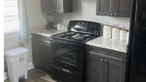 Una cocina con armarios oscuros, una estufa negra y un cubo de basura blanco.