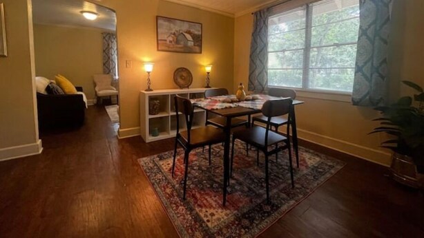 A dining area with a table, chairs, and a rug. There is a window with curtains and a plant on the right. - Peaceful Private home near VSU, Down town & SGMC (Valdosta)