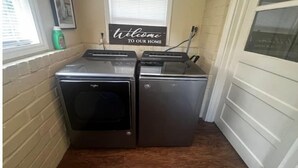 A laundry room with two stacked front-loading washers and dryers, a welcome sign above a window, and a door with a glass panel. - Peaceful Private home near VSU, Down town & SGMC (Valdosta)