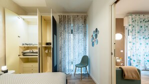 Ett sovrum med en säng, en stol, en garderob, ett skrivbord och ett badrum med en duschdraperi.
