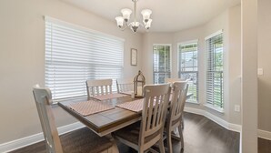 Uma sala de jantar com uma mesa de madeira, cadeiras brancas e um lustre.