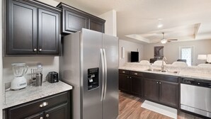 Cozinha moderna com armários escuros, eletrodomésticos de aço inoxidável, bancada de granito e ventilador de teto.