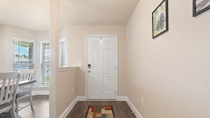 Um corredor com uma porta branca, uma sala de jantar com mesa e cadeiras, e um tapete estampado no chão.