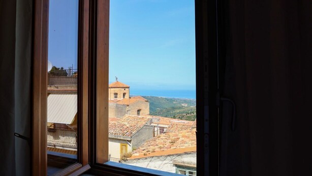 A view from a window overlooking a coastal town with terracotta-roofed buildings and a clear blue sky. - Le Signorine Panoramic apts: Donna Rosina (Gratteri)