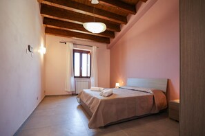 A bedroom with a bed, a nightstand, a window with curtains, and a wooden ceiling. - Le Signorine Panoramic apts: Donna Rosina (Gratteri)