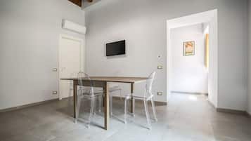 A modern dining area with a wooden table and clear chairs, a mounted TV, and a white door.