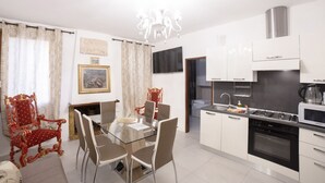 A modern kitchen with white cabinets, a gas stove, and a microwave. There is a dining area with a glass table and chairs, and a red ornate chair.