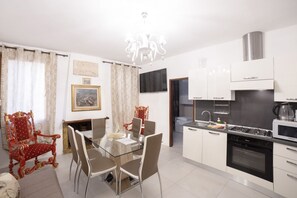 A modern kitchen with white cabinets, a gas stove, and a microwave. There is a dining area with a glass table and chairs, and a red ornate chair.