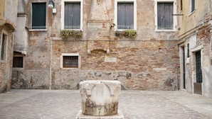 A courtyard with a stone fountain, brick walls, and windows with shutters.