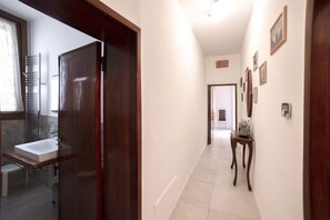 A hallway with a wooden door leading to a bathroom, a small table with a radio, and framed pictures on the wall.