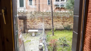 A courtyard with a stone bench, potted plants, and a brick wall.