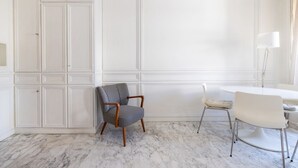 A room with a white marble floor, a white dining table with a white chair, and a patterned armchair.