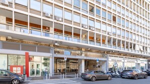 A multi-story building with a modern architectural design, featuring a large glass facade and a pedestrian crossing in front.
