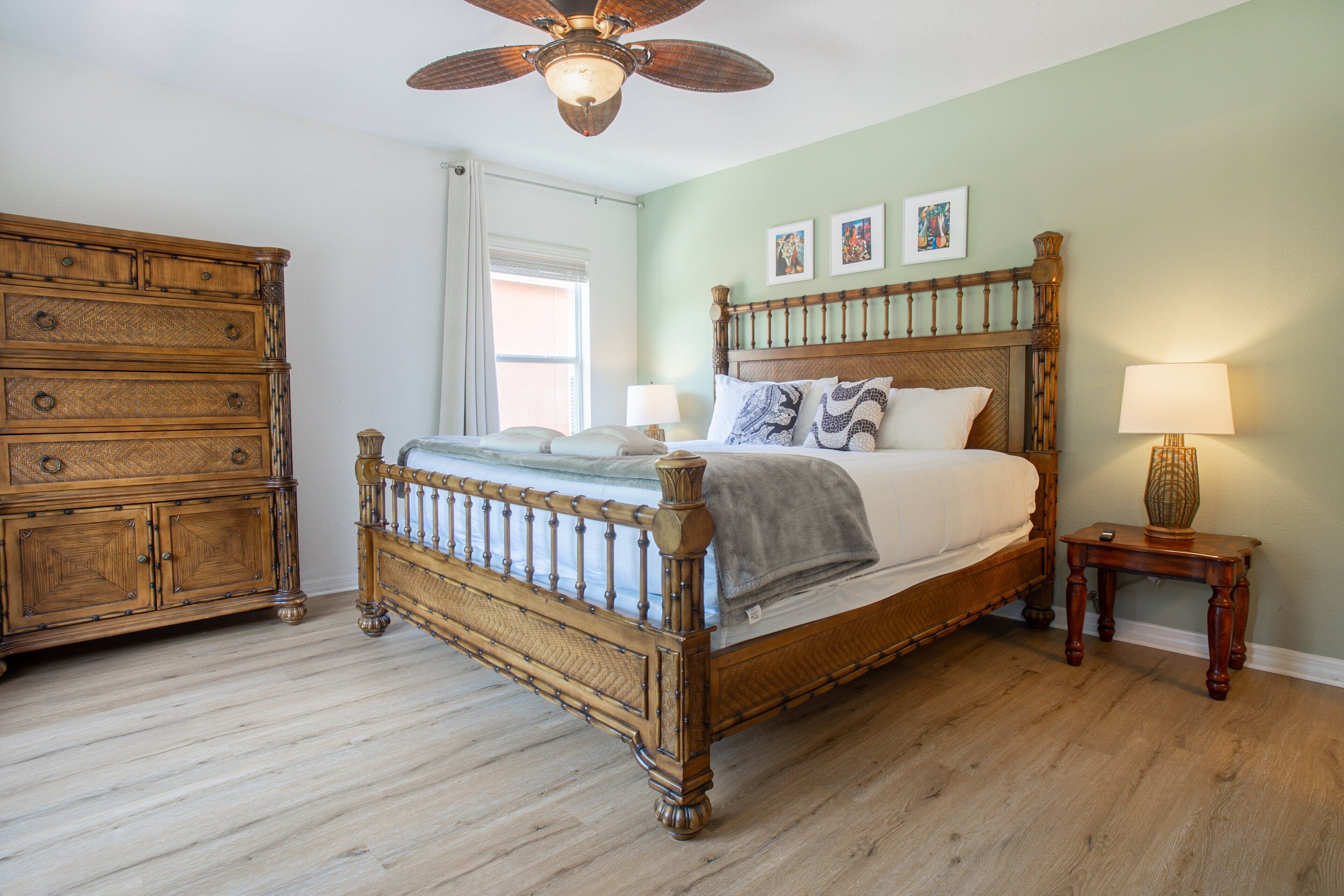 A bedroom with a wooden bed, a dresser, a nightstand with a lamp, and a ceiling fan.