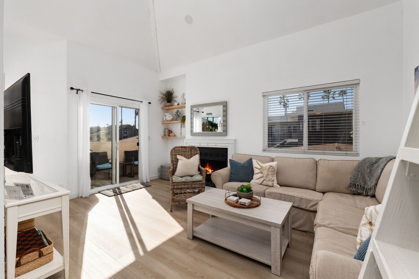 Una sala moderna con sofá, sillón y mesa de centro. Hay una chimenea, un televisor y un ventanal corredera que da a un área exterior.