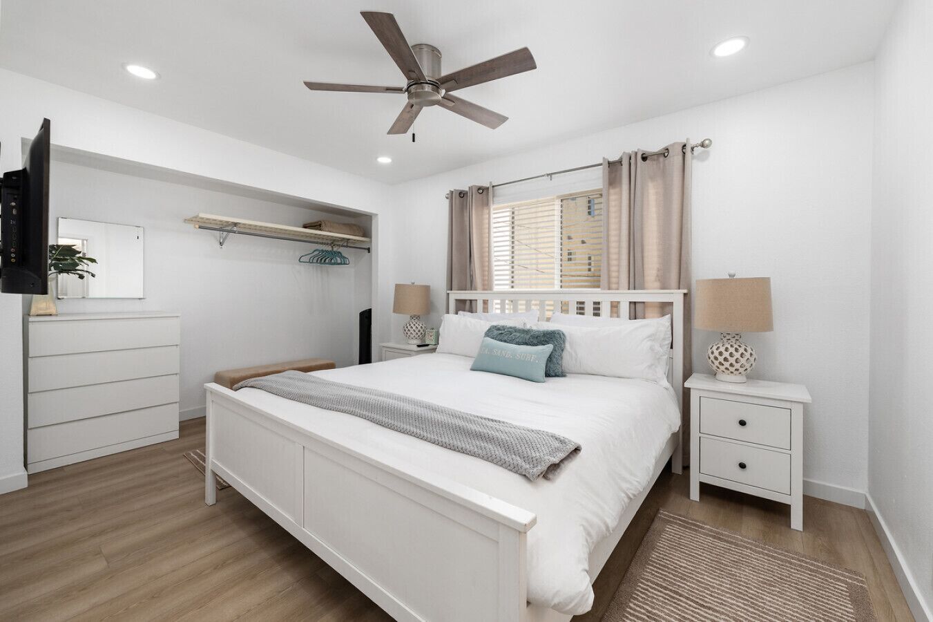 A modern bedroom with a bed, bedside tables, a ceiling fan, and a window with curtains.