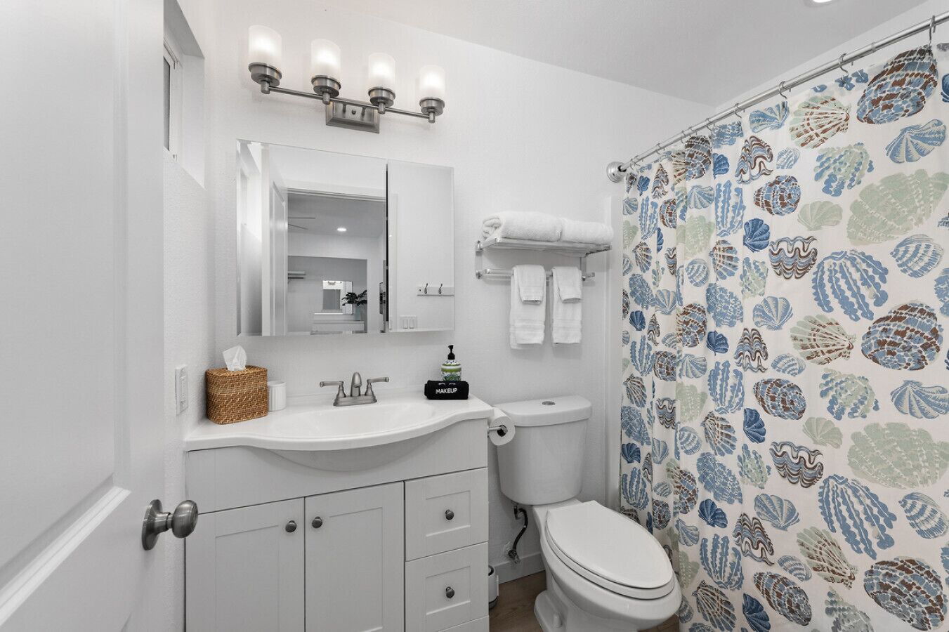 A bathroom with a white sink, mirror, and toilet. There is a shower curtain with a shell pattern.