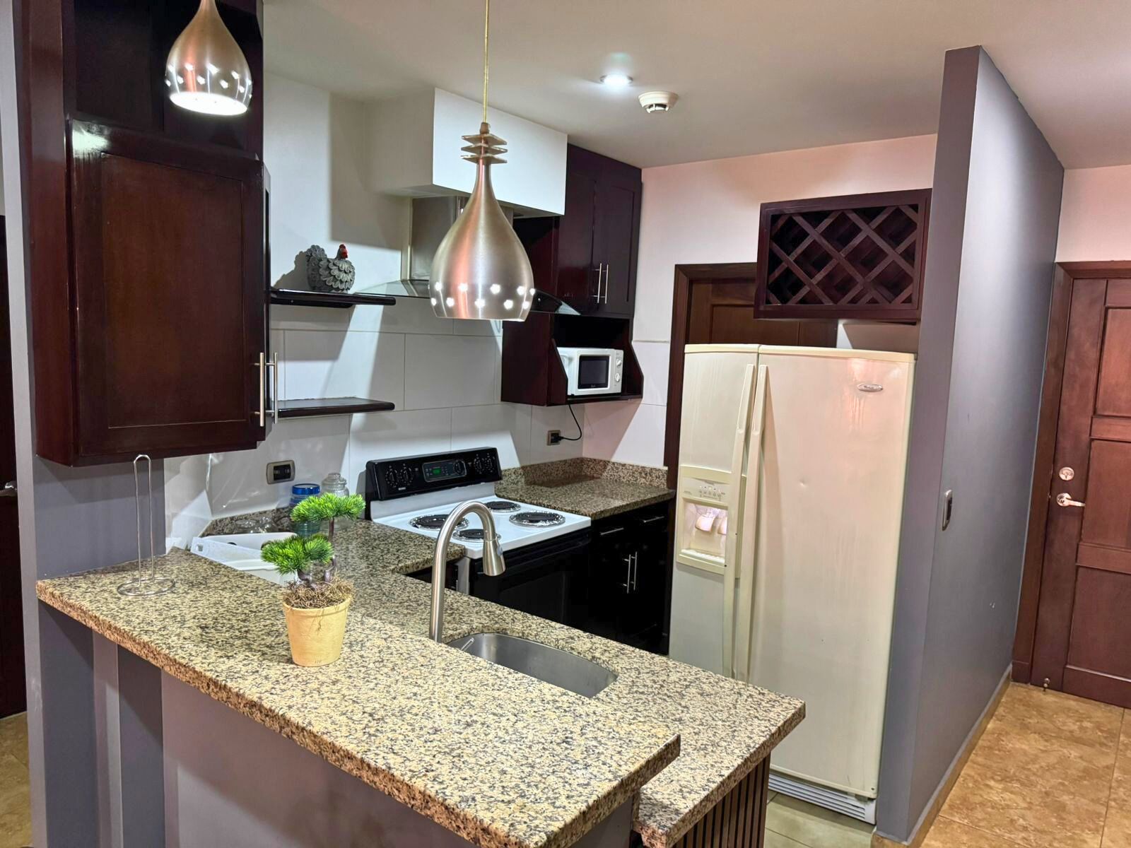 Une cuisine dotée de plans de travail en granit, d’une cuisinière, d’un évier, d’un réfrigérateur et de luminaires suspendus.