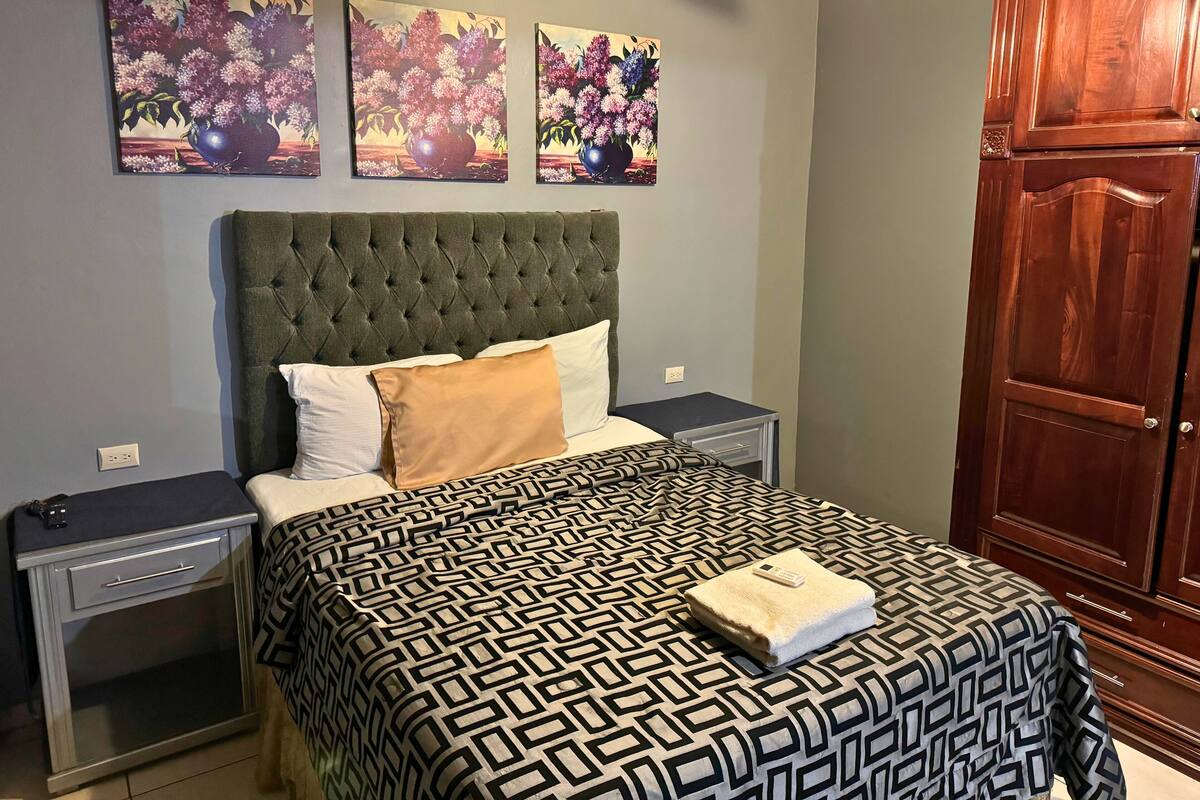 Une chambre à coucher avec une tête de lit capitonnée, une couvre-lit à motifs et trois tableaux accrochés au mur.