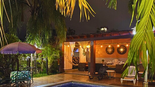 A swimming pool with a tiled edge, surrounded by palm trees and outdoor furniture. - Apartamentos Casa del Valle (San Pedro Sula)