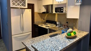 A compact kitchen with a refrigerator, stove, microwave, and granite countertop. - Apartamentos Casa del Valle (San Pedro Sula)