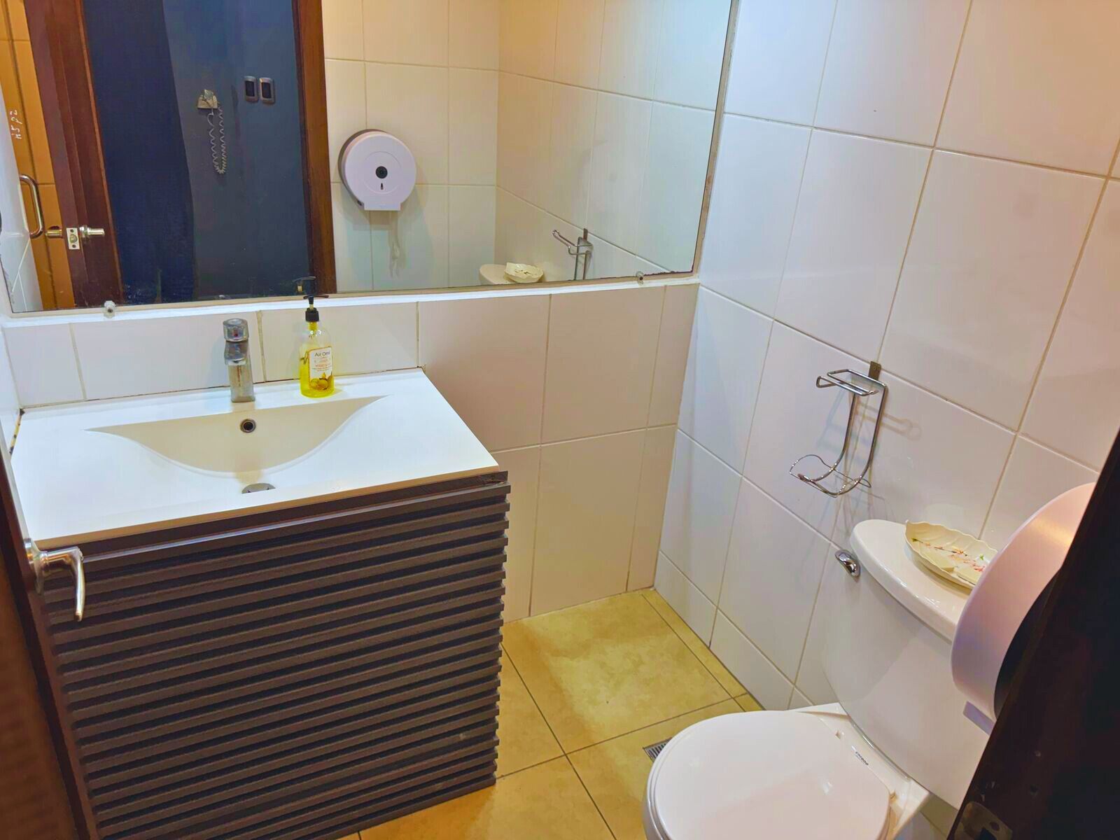 A bathroom with a white sink, a toilet, a mirror, and a soap dispenser.