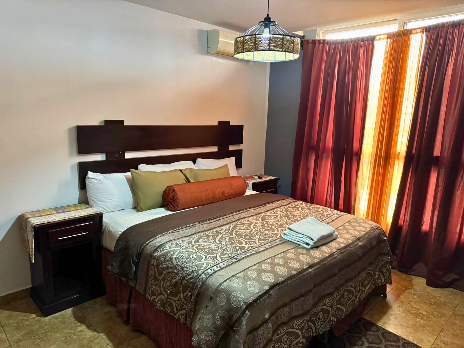 A hotel room with a bed, a nightstand, a lamp, and a window with curtains.