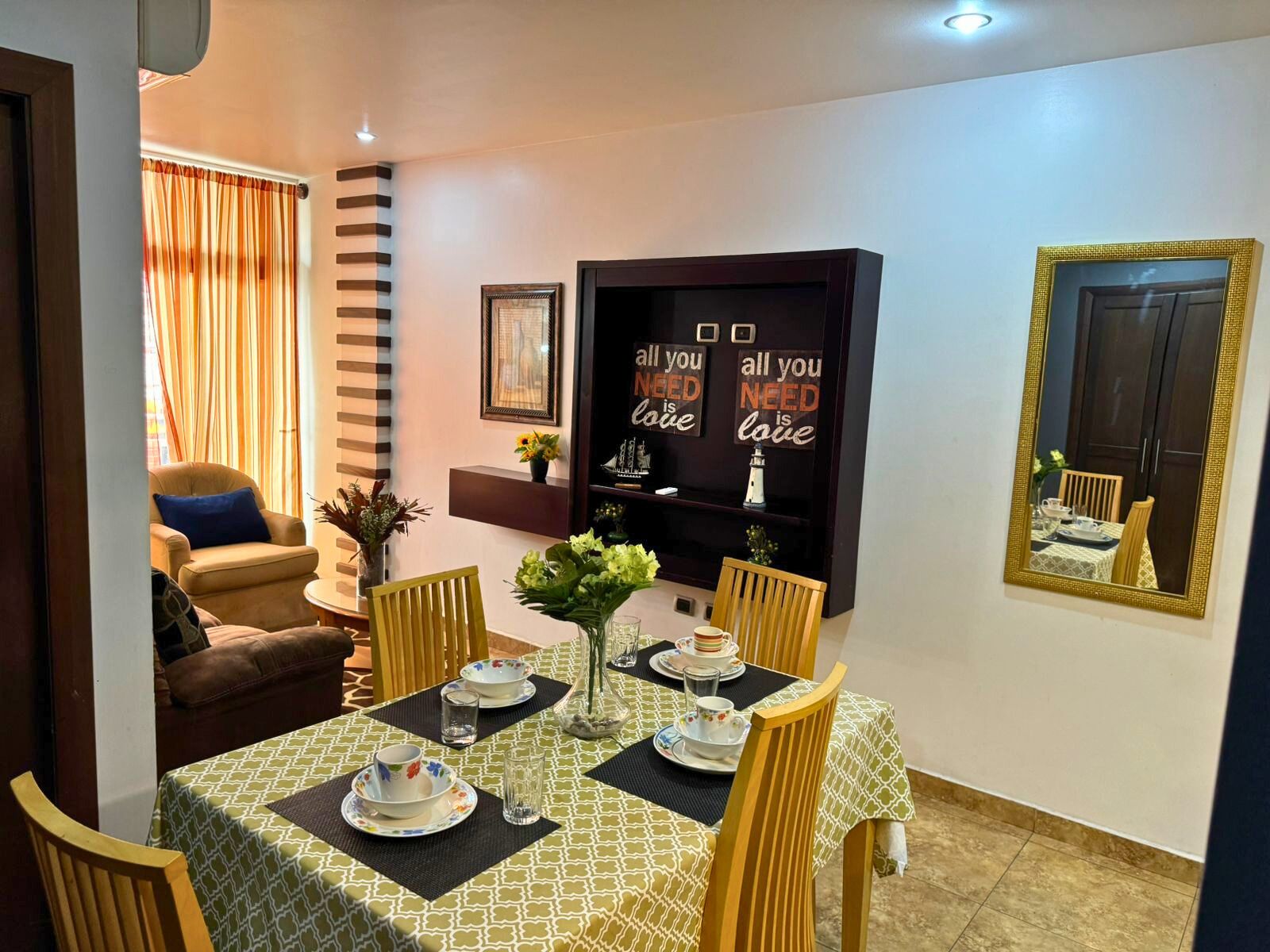 Un coin repas avec une table dressée pour quatre personnes, des chaises, un canapé, une bibliothèque et un miroir.