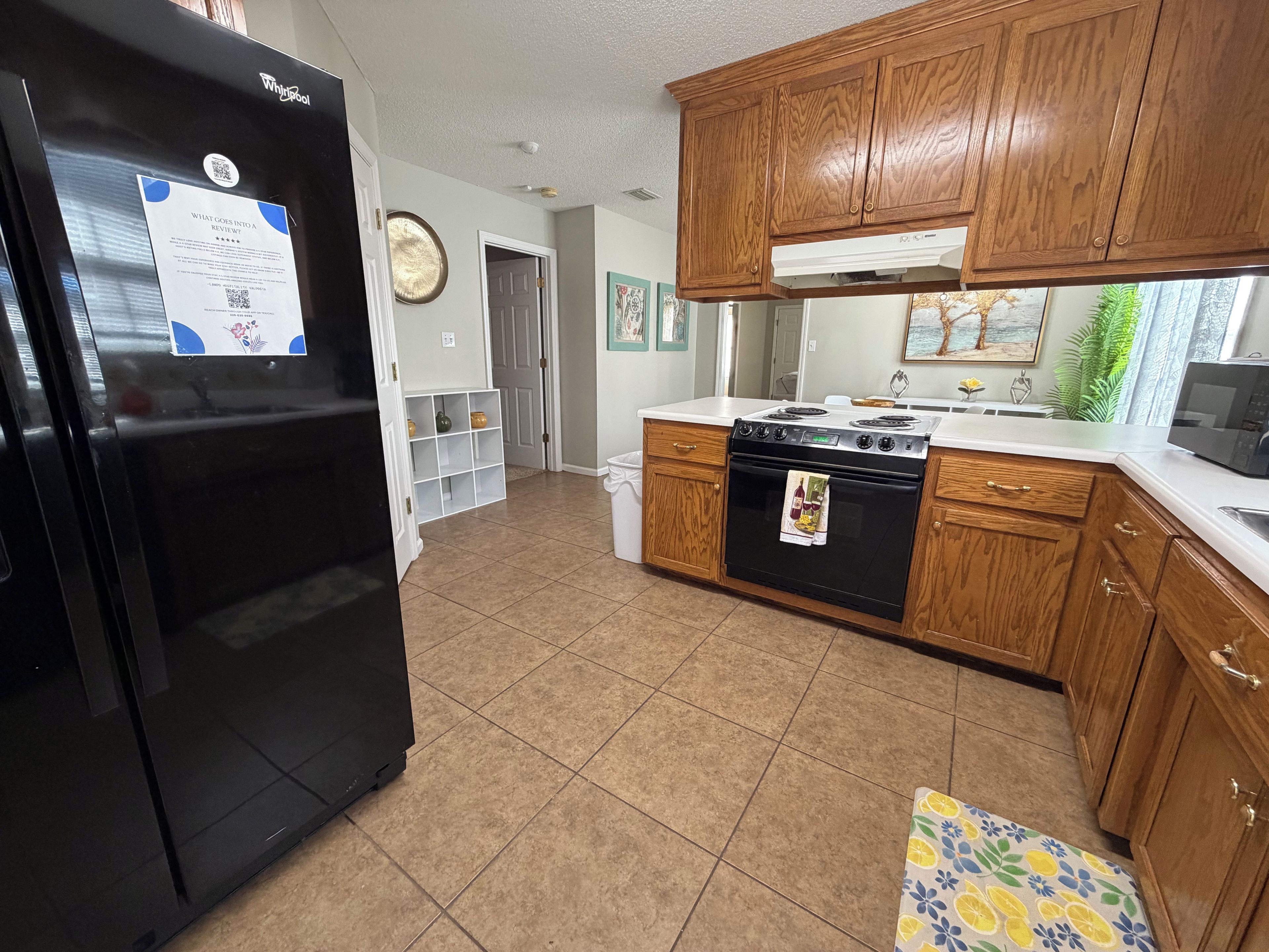 A kitchen with a black Whirlpool refrigerator, wooden cabinets, a white countertop, and a stove.