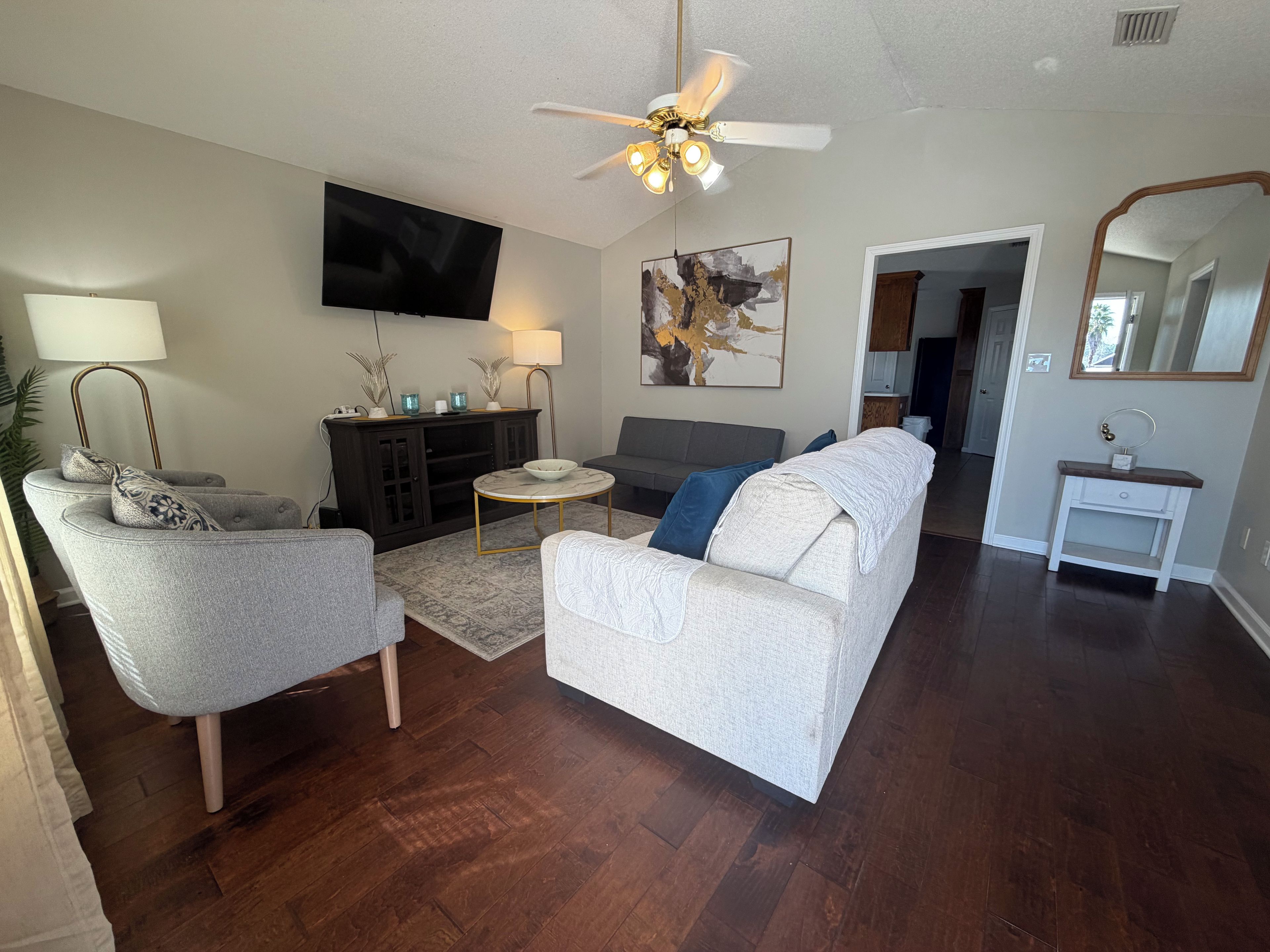 A living room with a flat-screen TV, a ceiling fan, a sofa, a coffee table, and a side table.
