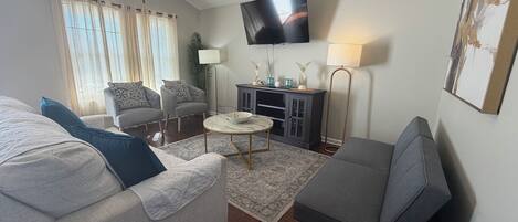 A living room with a sofa, armchair, coffee table, TV, and a ceiling fan.