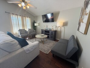 A living room with a sofa, armchair, coffee table, TV, and a ceiling fan.
