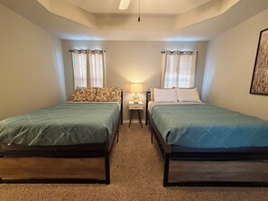 Une chambre avec deux lits simples, une table de chevet avec une lampe et une fenêtre avec des rideaux.