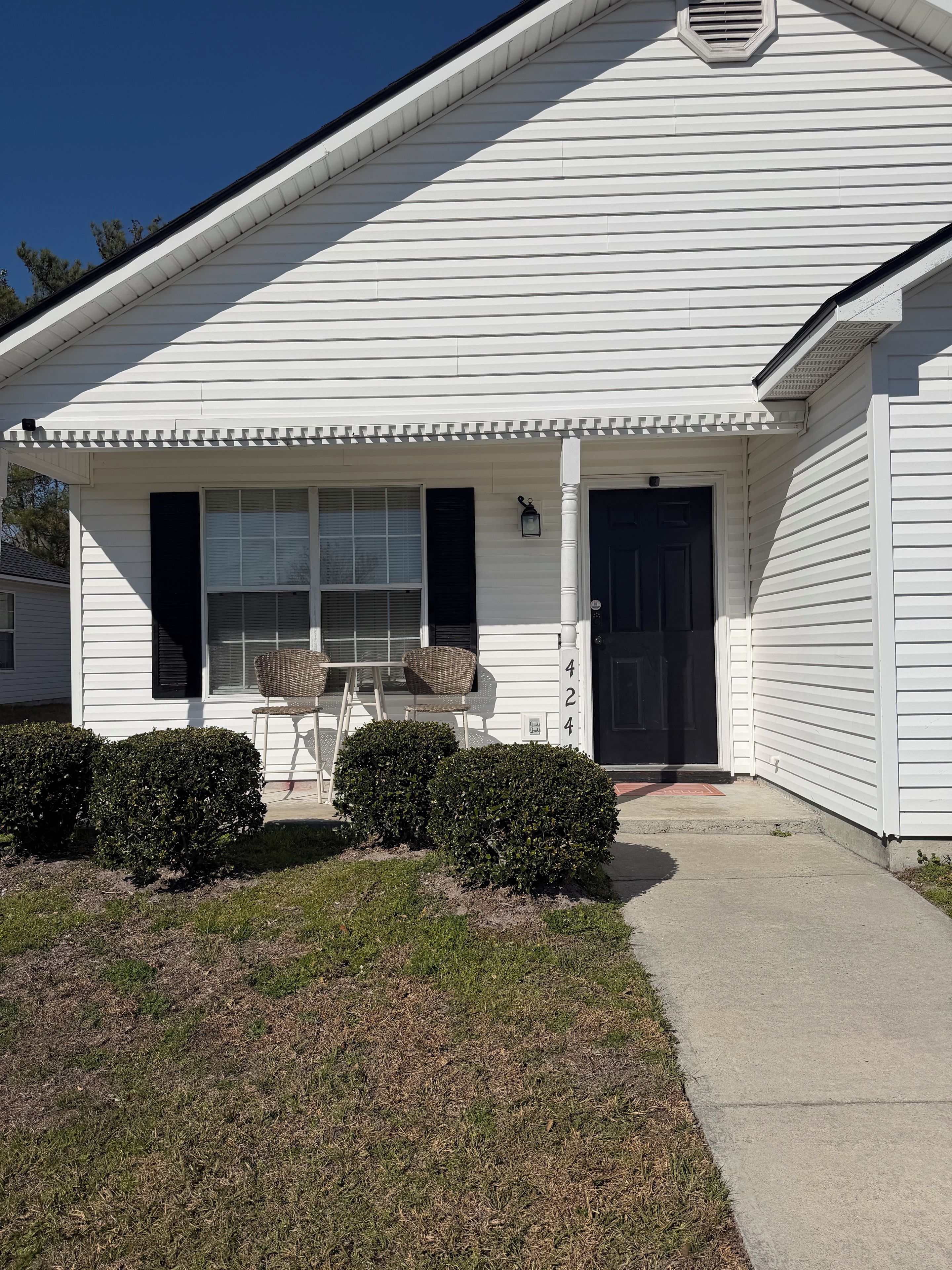 A white single-story house with a front porch, two windows with shutters, a door, and a small number '424' sign.