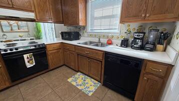 Una cocina con armarios de madera, estufa, microondas, lavavajillas y una ventana con persianas.