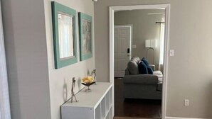 Un pasillo con un sofá gris al fondo, una consola blanca con objetos decorativos y un piso de baldosas.
