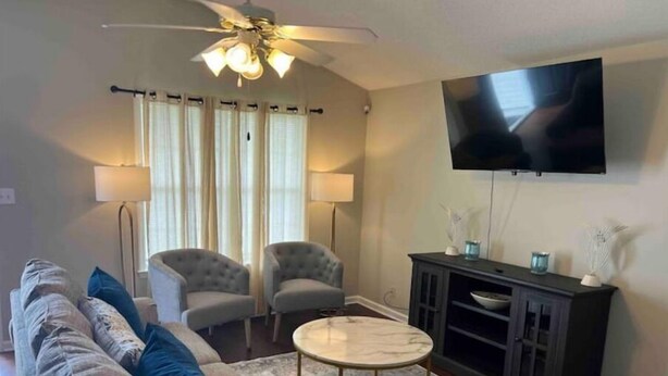 Una sala de estar con un sofá, dos sillones, una mesa de centro, un televisor y un ventilador de techo.