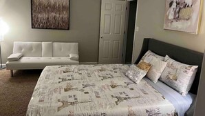 A bedroom with a large bed, a white sofa, a ceiling fan, and two doors. - Peaceful Private Home near Moody, Wild Adventures (Valdosta)